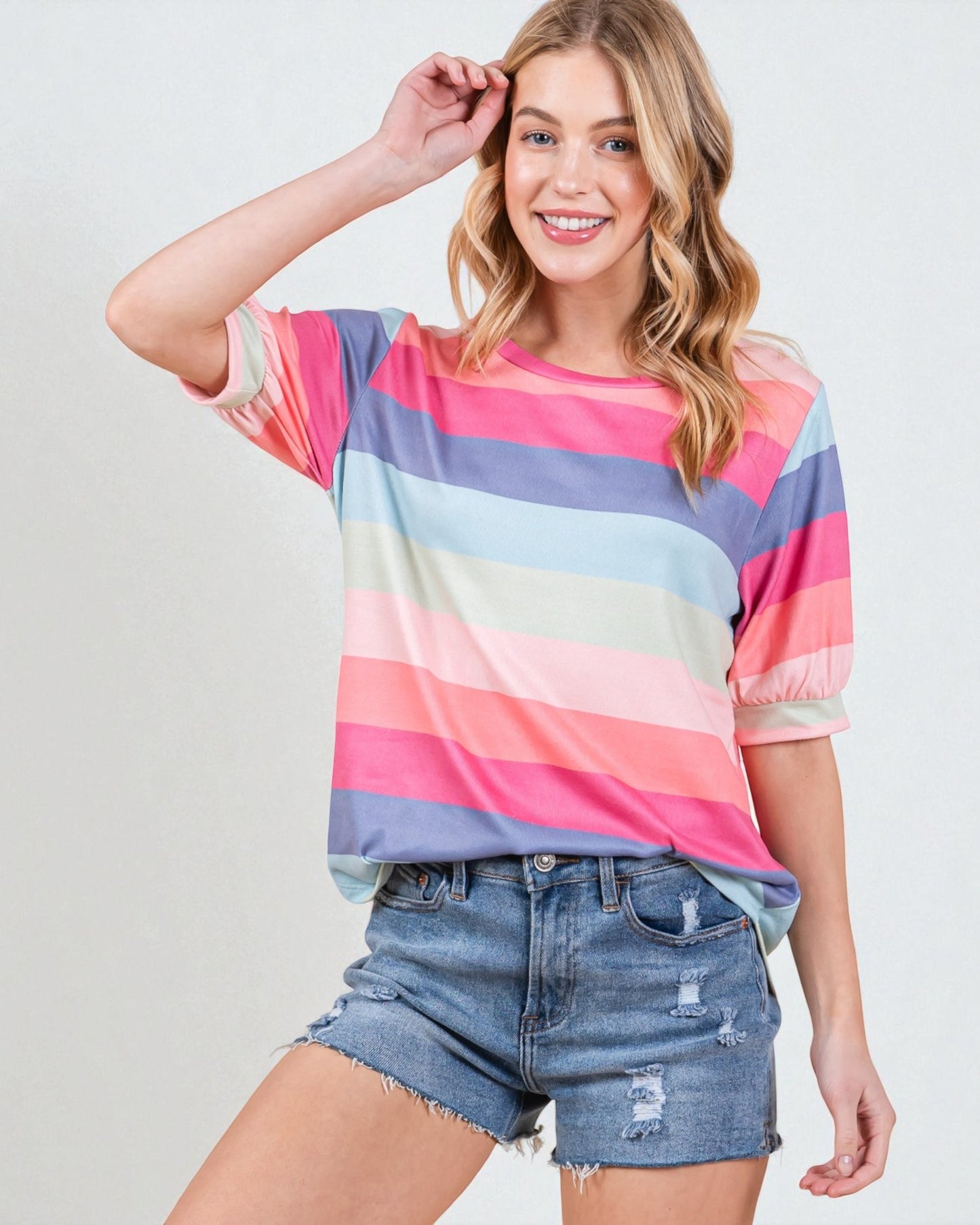 Woman wearing a colorful striped shirt and denim shorts on a plain background