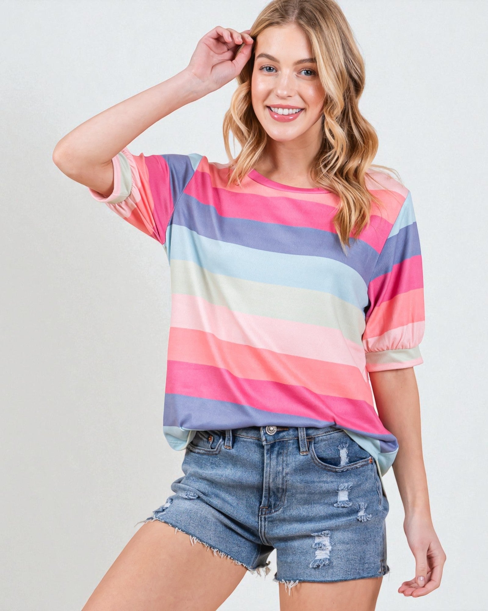 Woman wearing a colorful striped shirt and denim shorts on a plain background