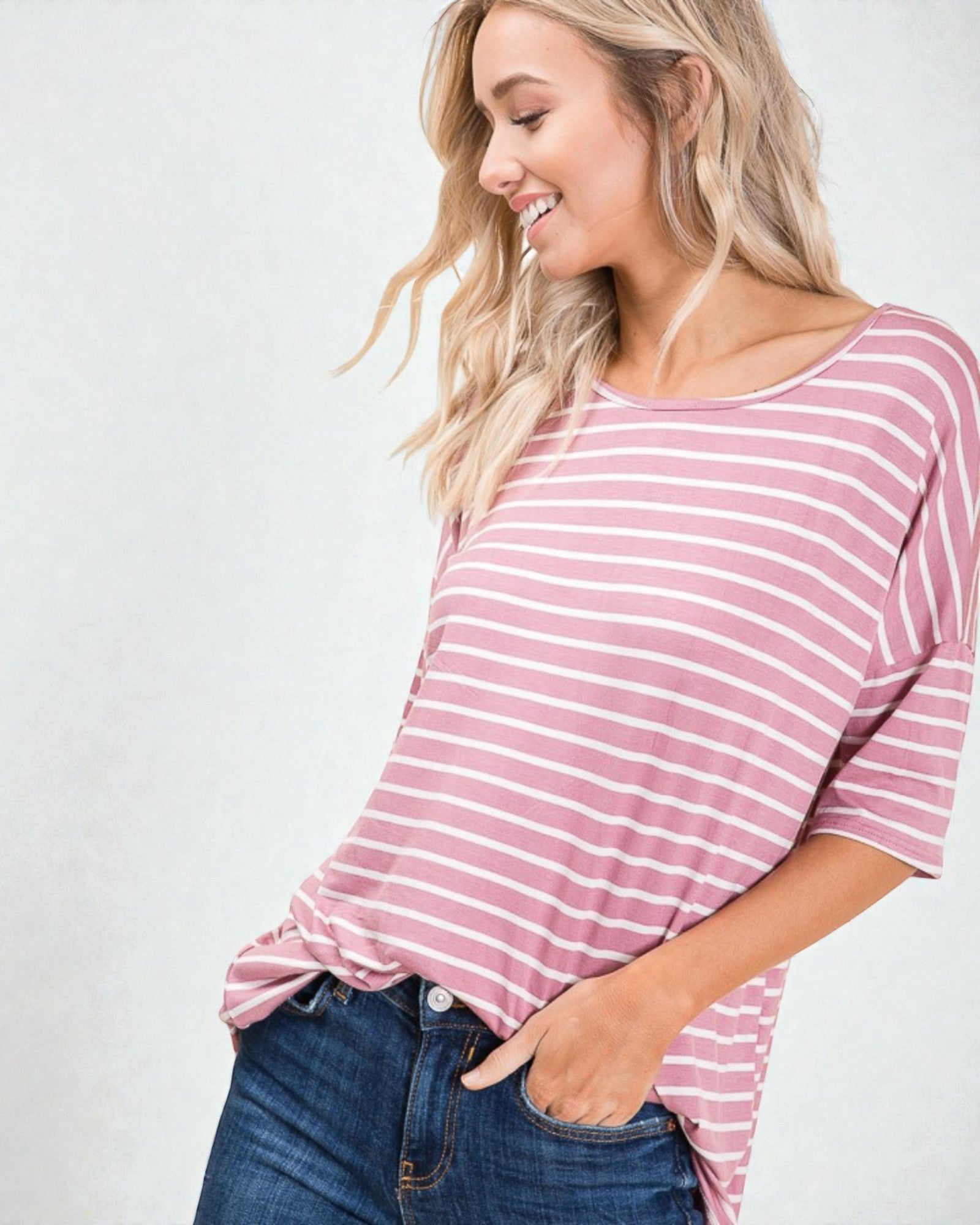 Woman wearing a pink and white striped shirt with blue jeans on a plain background