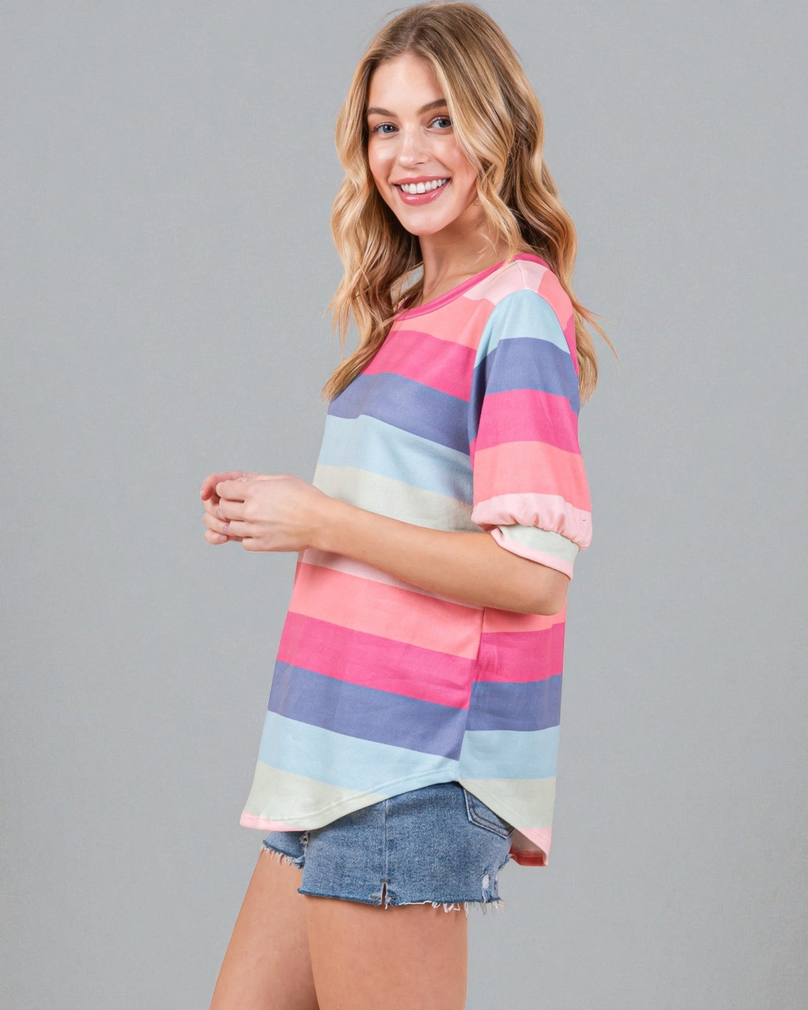 Woman wearing a colorful striped shirt and denim shorts on a gray background