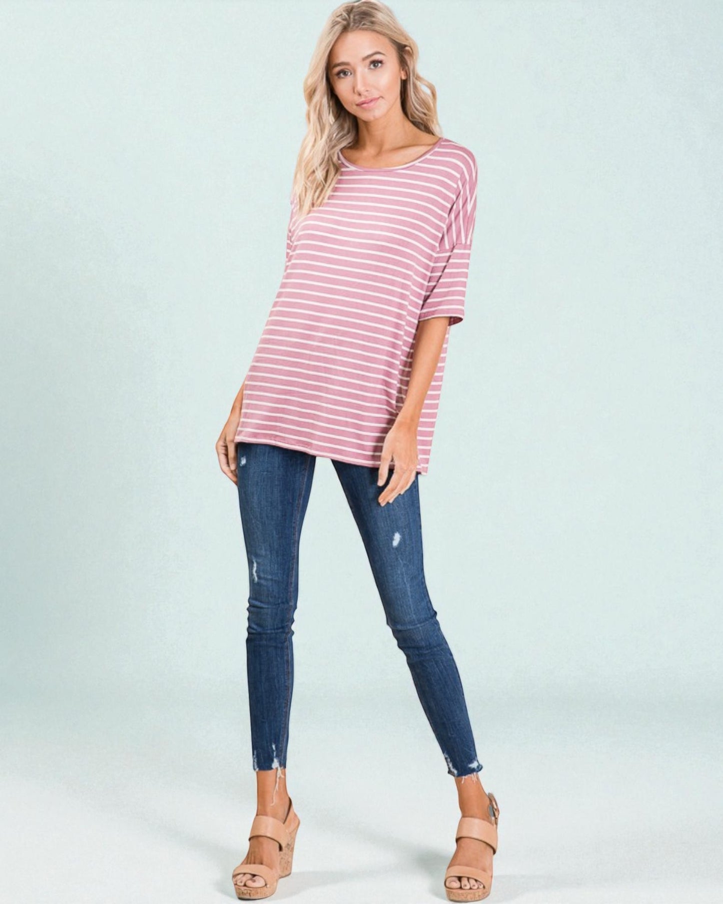 Woman wearing a pink and white striped top and blue jeans on a light gray background