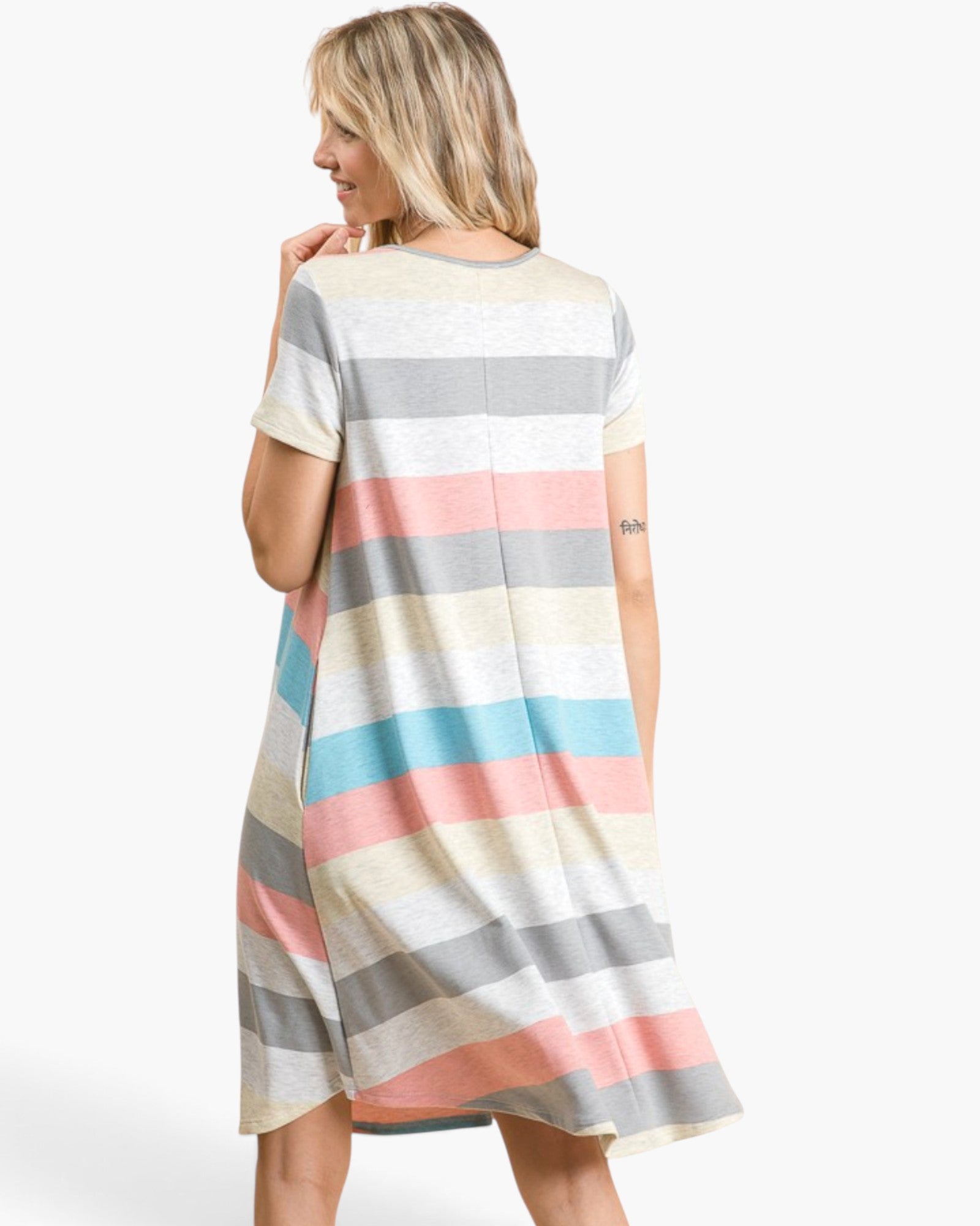 A woman wearing a short-sleeve, A-line shift dress with horizontal pastel stripes in cream, gray, pink, and light blue, shown from a back-three-quarter view against a plain white studio background.