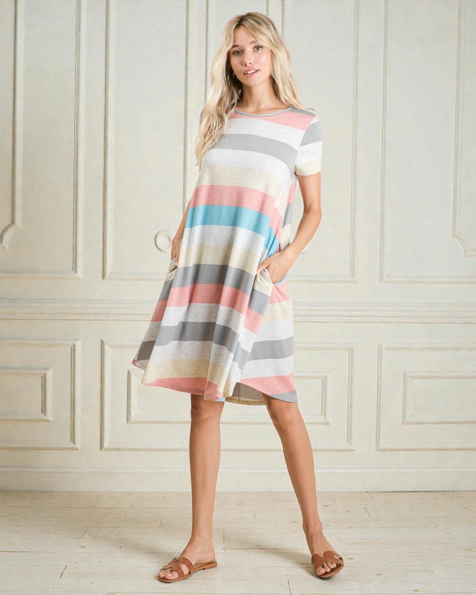 Woman wearing a striped dress standing against a white paneled wall.