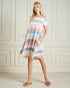 Woman wearing a striped dress standing against a white paneled wall.