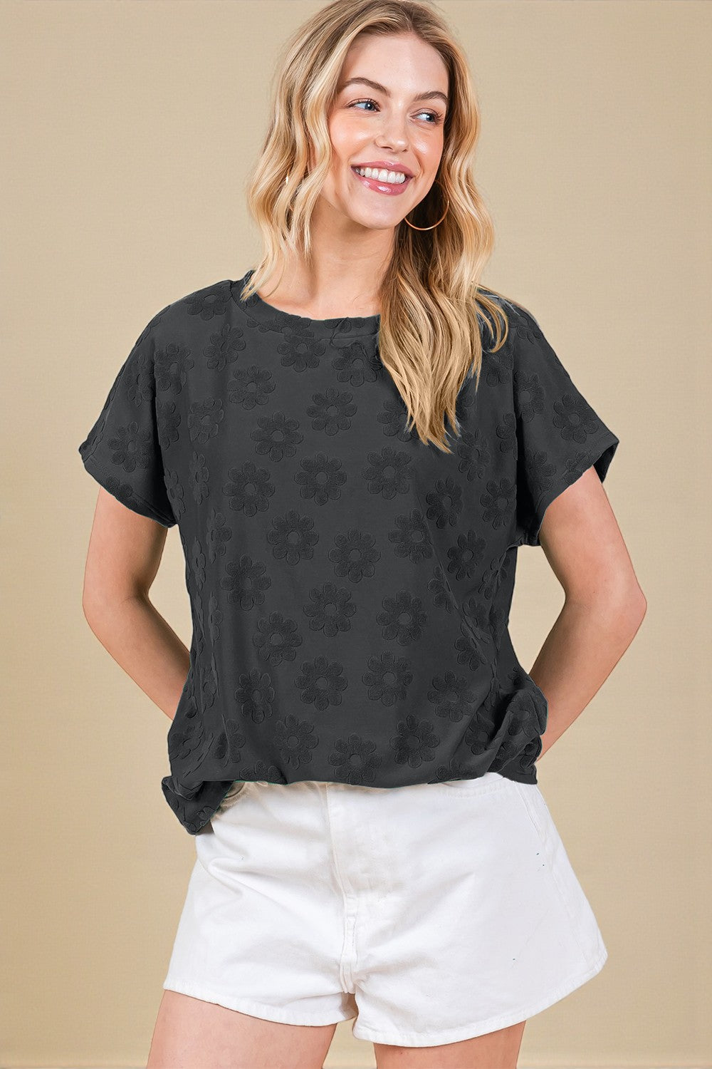 Woman wearing a black patterned top and white shorts against a beige background