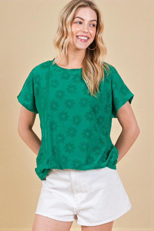 Woman wearing a green patterned top and white shorts against a beige background