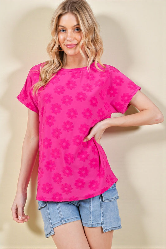 Woman wearing a bright pink floral-patterned top and denim shorts on a beige background