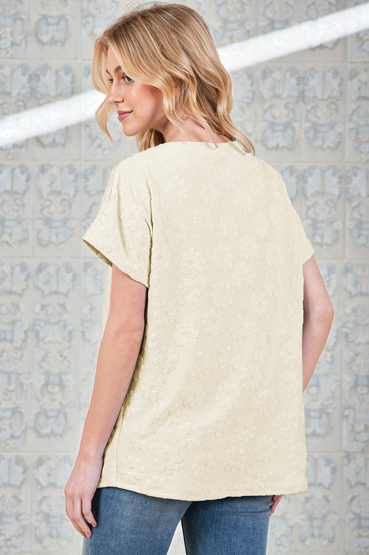 Woman wearing a light-colored t-shirt and blue jeans against a textured wall.