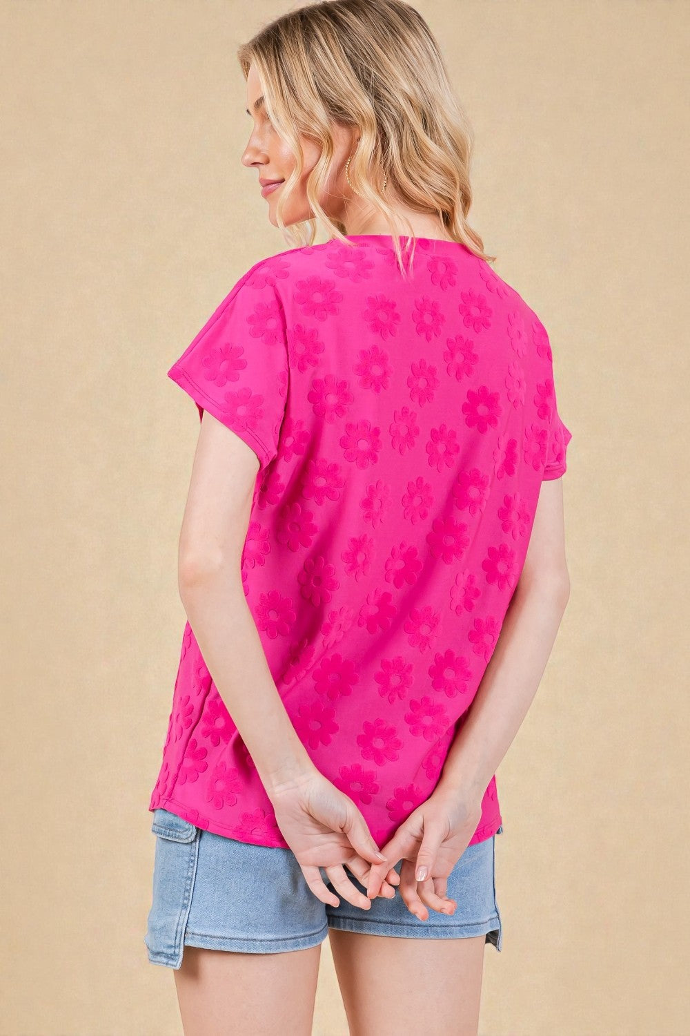 Woman wearing a bright pink floral-patterned top and denim shorts on a beige background