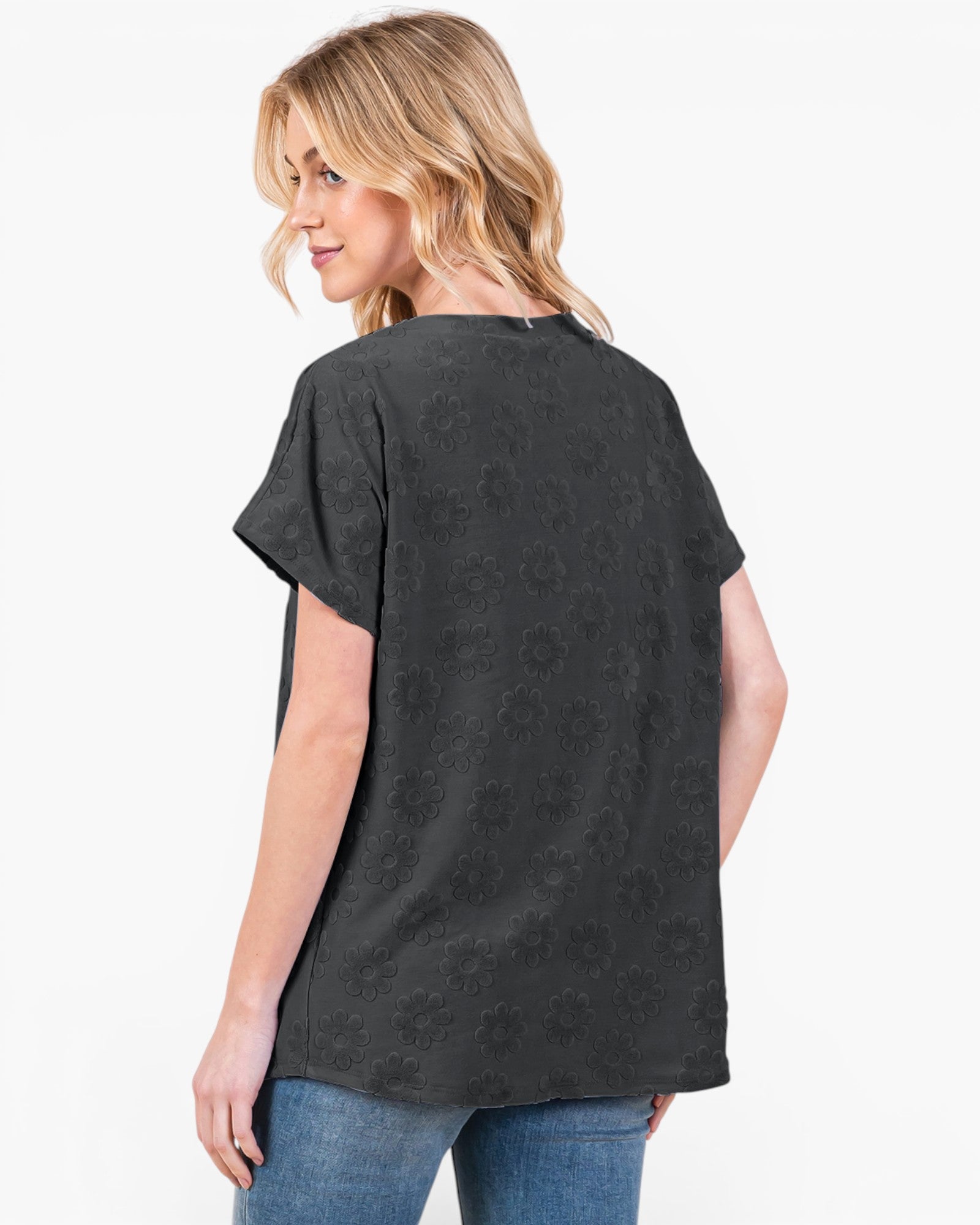 A woman shown from the back wearing a black short-sleeve top with a subtle tonal floral jacquard pattern, paired with blue jeans, against a plain white background.