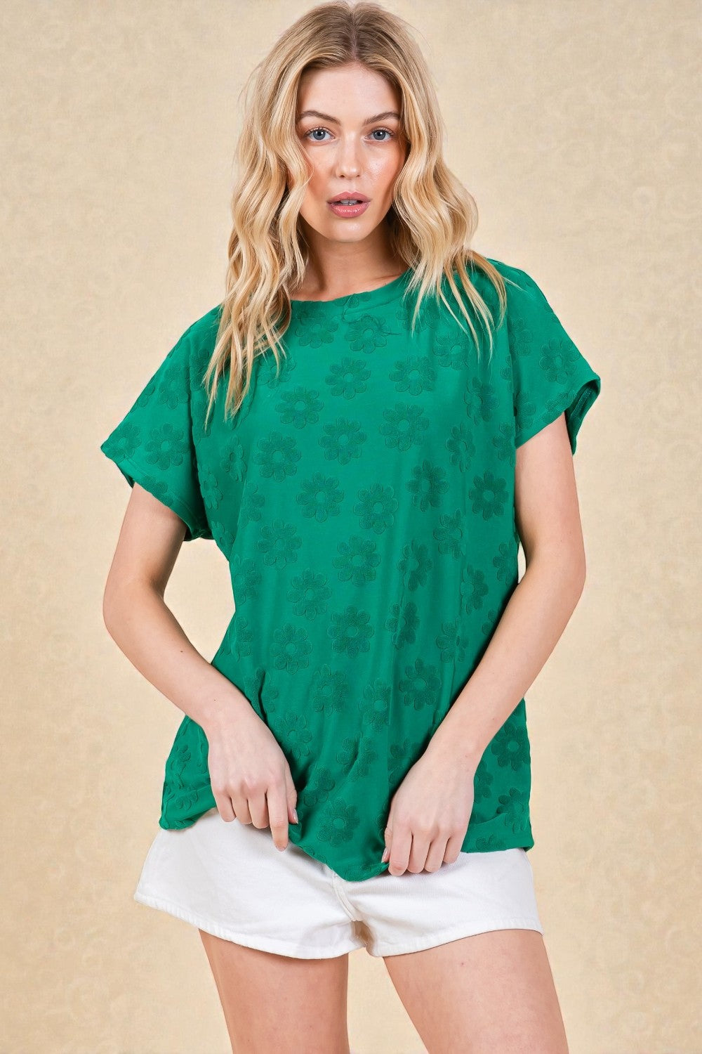 Woman wearing a green patterned top and white shorts on a beige background