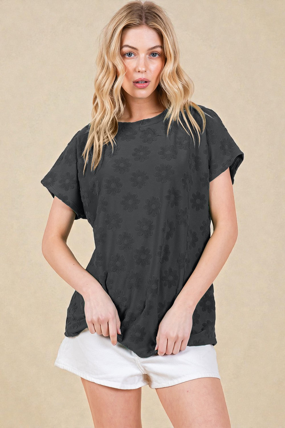 Woman wearing a black floral patterned top and white shorts on a beige background