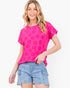 A woman wearing a bright pink short-sleeve t-shirt with a tonal floral pattern and light-wash denim shorts, standing against a plain white studio background.