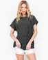 A woman modeling a dark charcoal gray short-sleeve t-shirt with a subtle tonal floral pattern, paired with white shorts, against a plain white studio background.