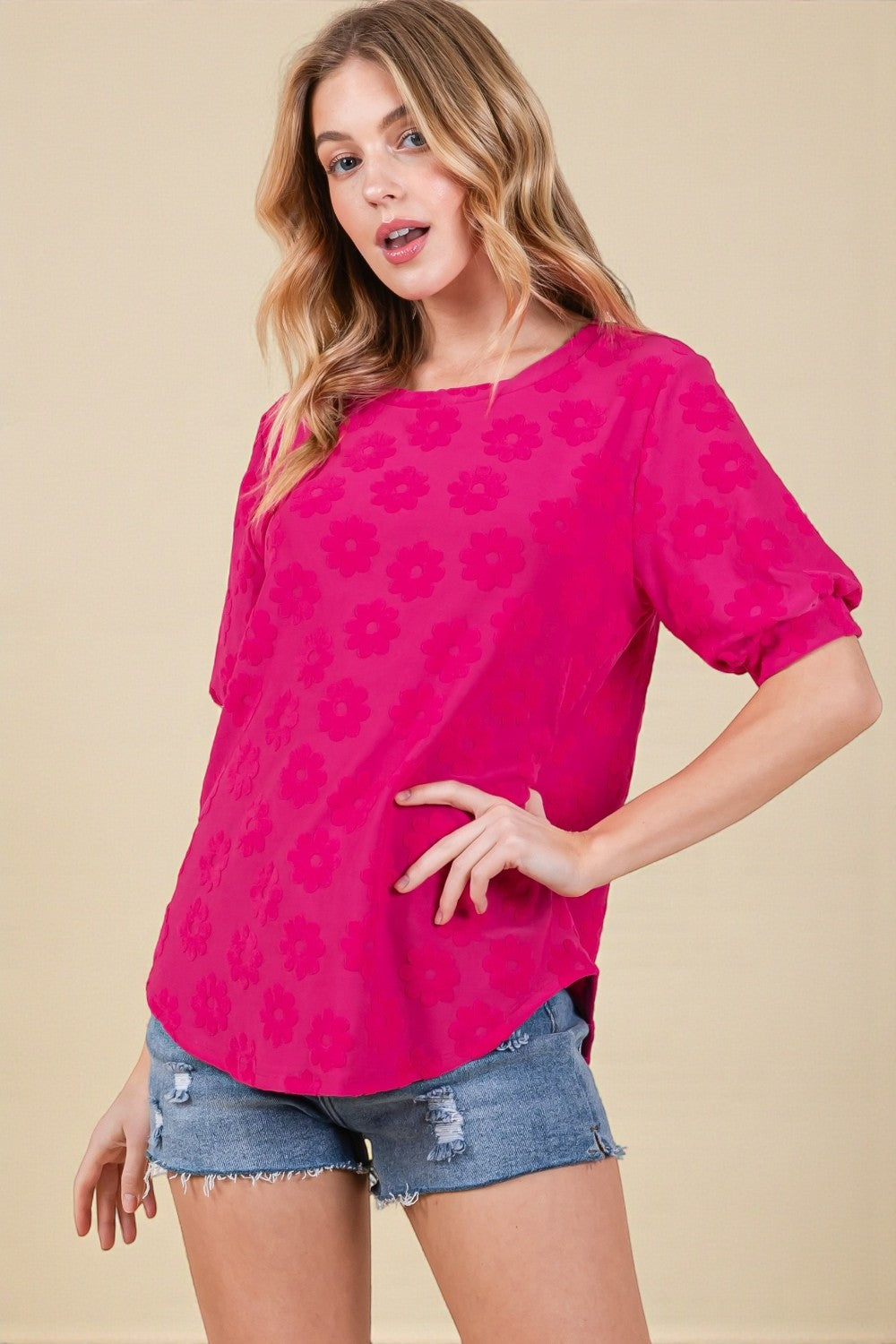 Woman wearing a bright pink floral blouse and denim shorts on a beige background