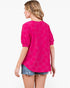 A woman shown from the back wearing a bright pink short-sleeve top with a tonal floral pattern and denim shorts against a plain white background.