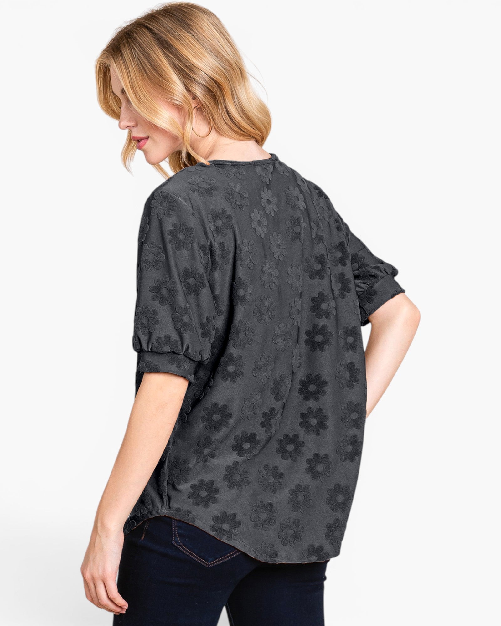 A woman shown from the back wearing a dark gray short-sleeve blouse with a tonal floral jacquard pattern, paired with dark blue jeans, against a plain white background.