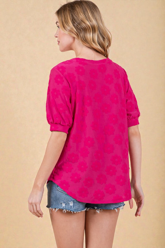 Woman wearing a bright pink floral blouse with denim shorts on a beige background