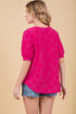 Woman wearing a bright pink floral blouse with denim shorts on a beige background