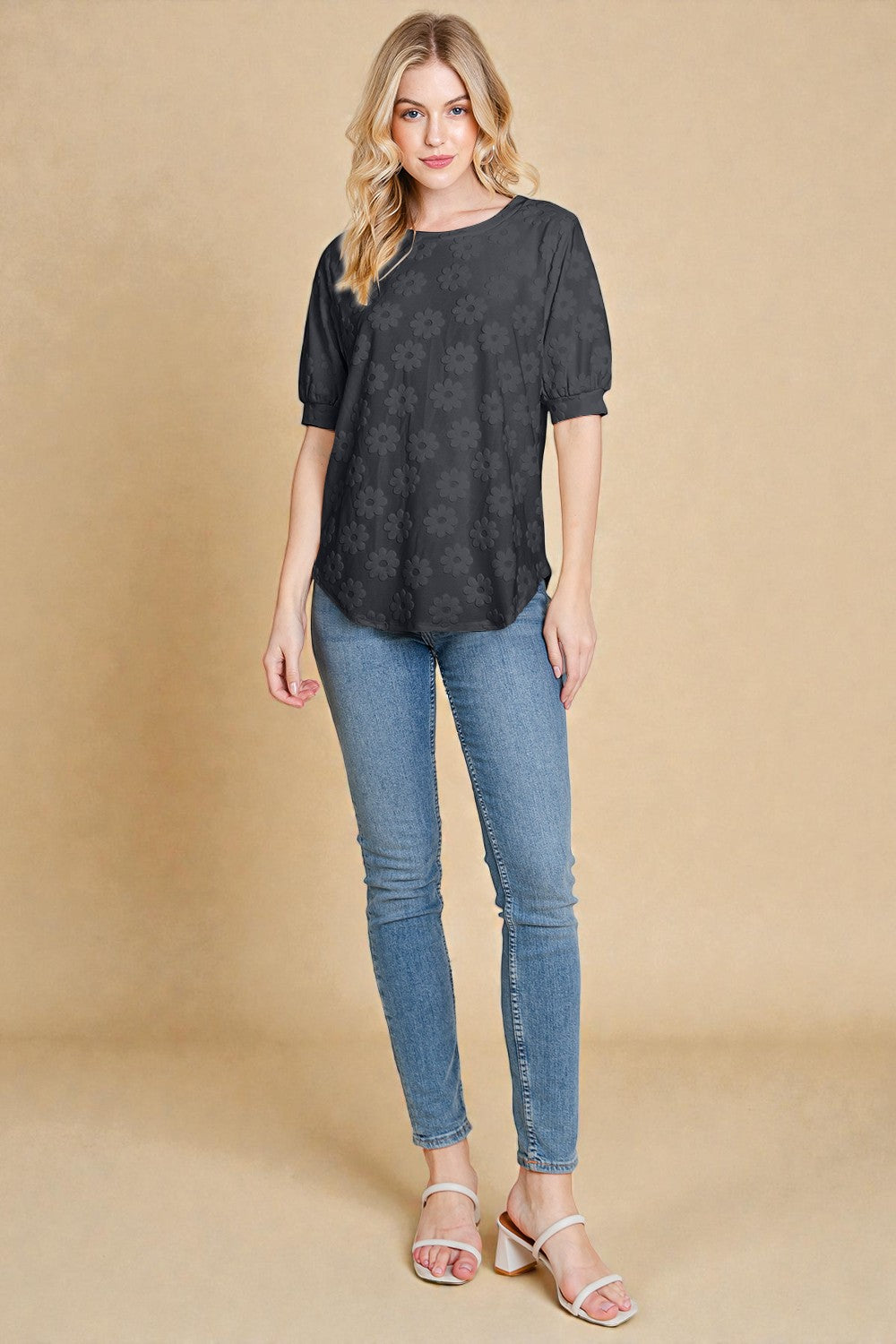 Woman wearing a black patterned top and blue jeans on a beige background