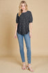 Woman wearing a black patterned top and blue jeans on a beige background