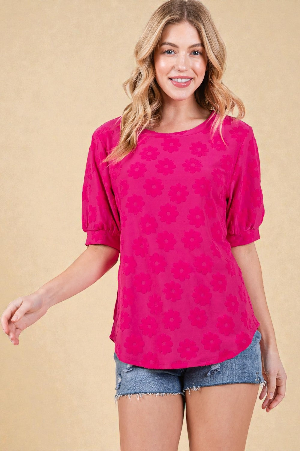 Woman wearing a pink floral blouse and denim shorts on a beige background