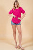Woman wearing a bright pink top and denim shorts on a beige background