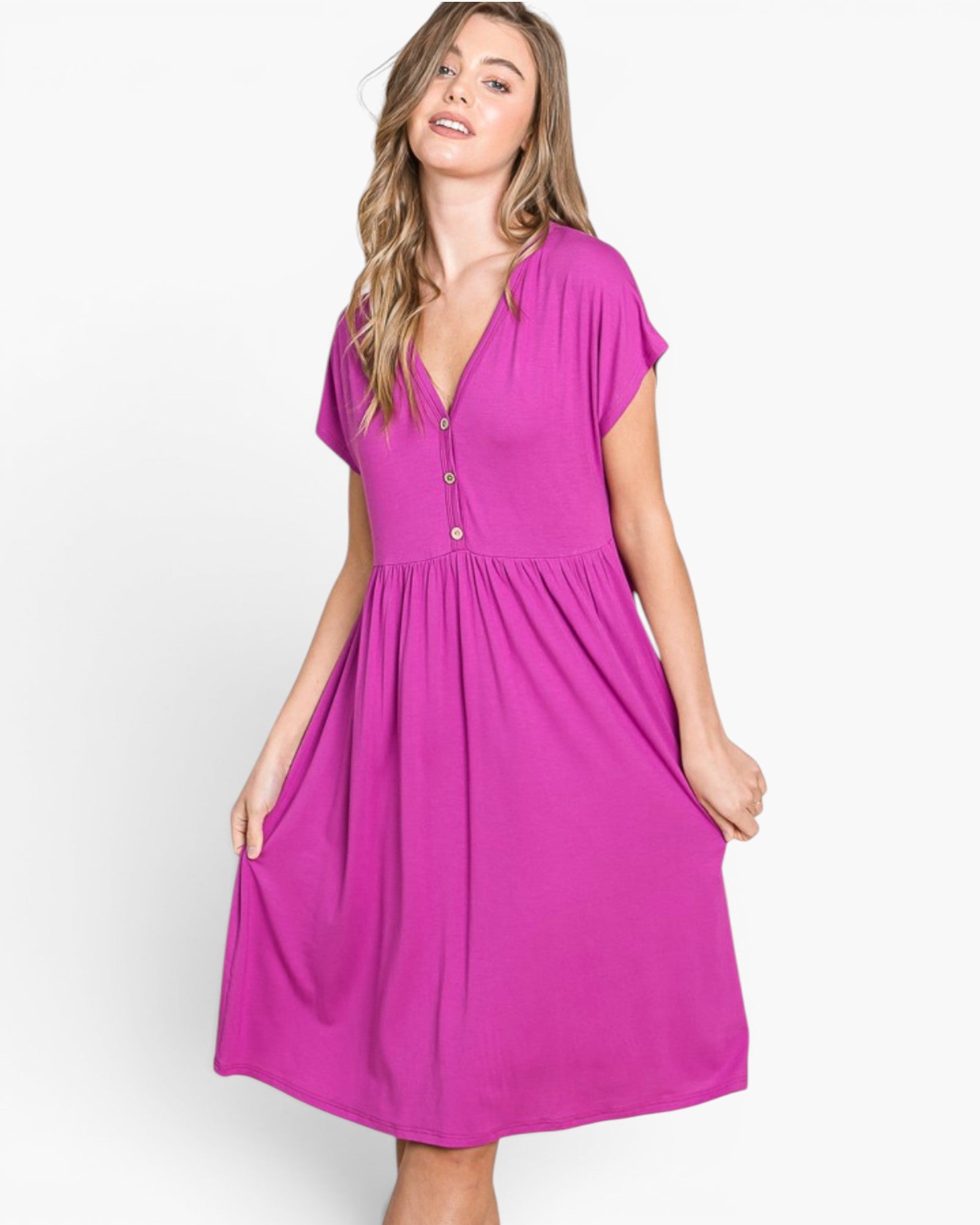 A woman modeling a bright magenta midi dress with short sleeves, a V-neckline with front buttons, and a gathered waist, set against a plain light gray studio background.