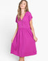 A woman modeling a bright magenta midi dress with short sleeves, a V-neckline with front buttons, and a gathered waist, set against a plain light gray studio background.