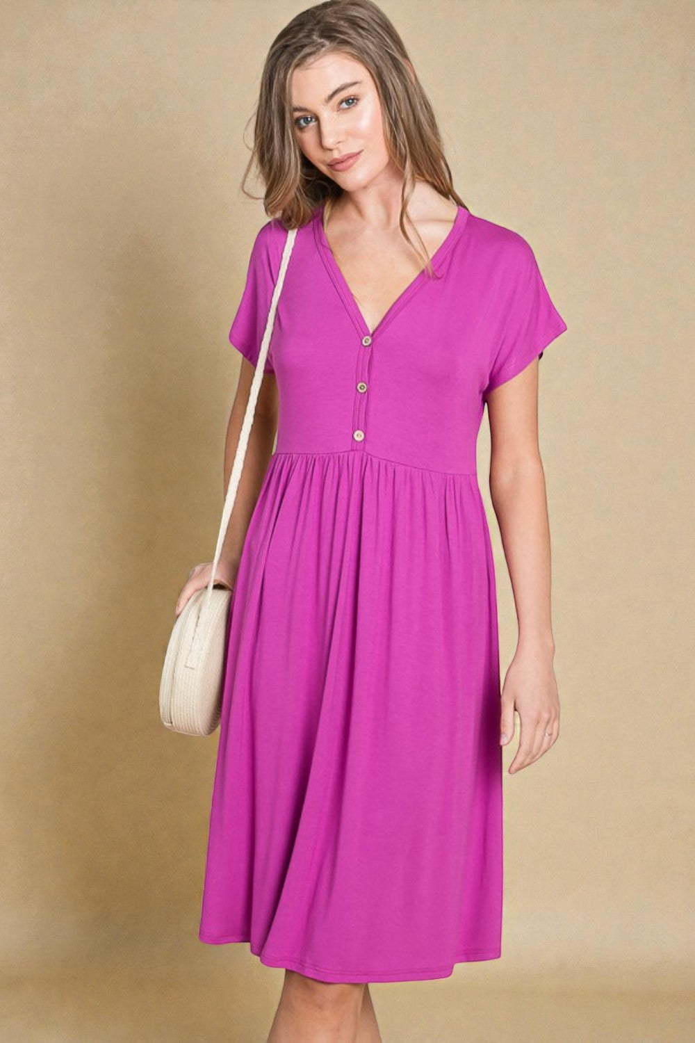 Woman wearing a pink dress holding a beige handbag against a beige background