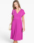 A woman modeling a bright magenta short-sleeve midi dress with a V-neck and button placket, carrying a small cream shoulder bag against a light gray studio background.