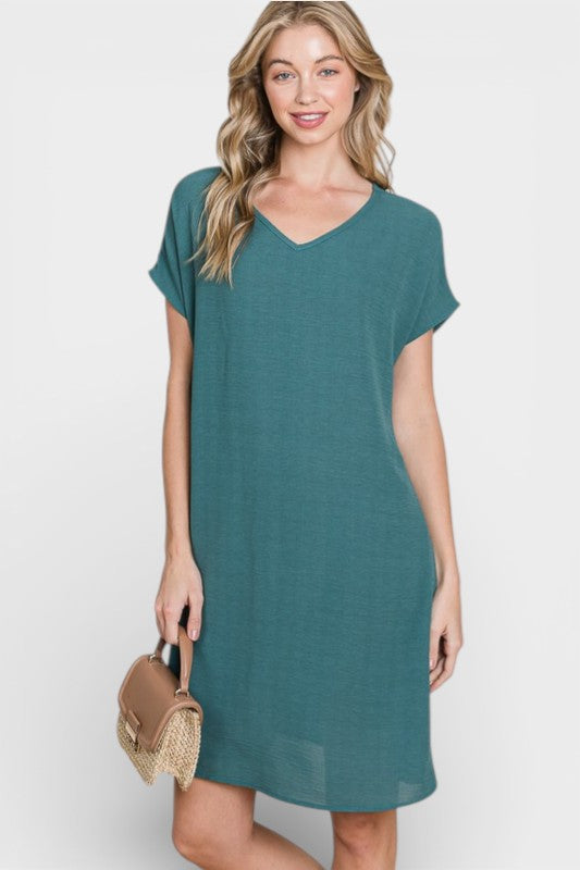 Woman wearing a teal dress holding a small bag on a white background