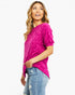 A woman wearing a bright pink short-sleeve top with a subtle tonal pattern, paired with light blue jeans, photographed against a plain white background.