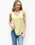 A woman wearing a pale yellow sleeveless tank top with a criss-cross neckline detail, paired with blue jeans, against a plain white studio background.