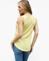 A woman wearing a pale yellow sleeveless tank top and blue jeans, shown from a side-back angle against a plain white studio background.