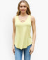 A woman modeling a pale yellow sleeveless tank top with a criss-cross cutout at the neckline, paired with blue jeans, against a plain white background.
