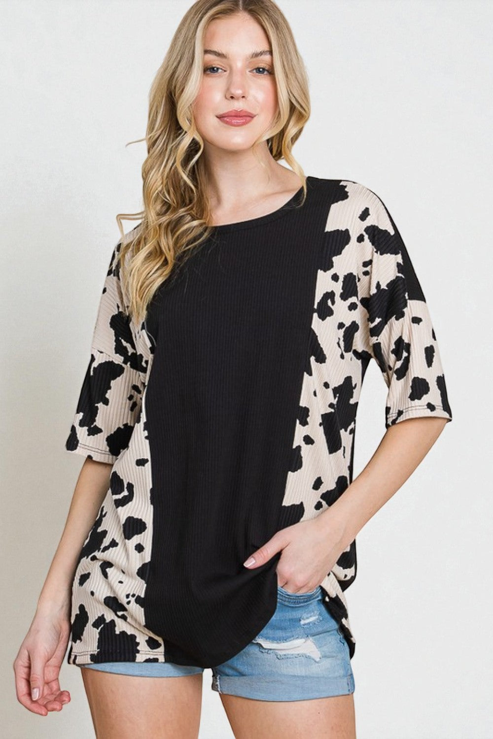 Woman wearing a black and beige cow print top with denim shorts on a white background