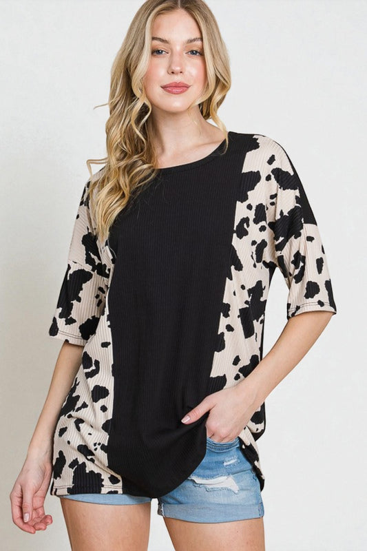 Woman wearing a black and beige cow print top with denim shorts on a white background