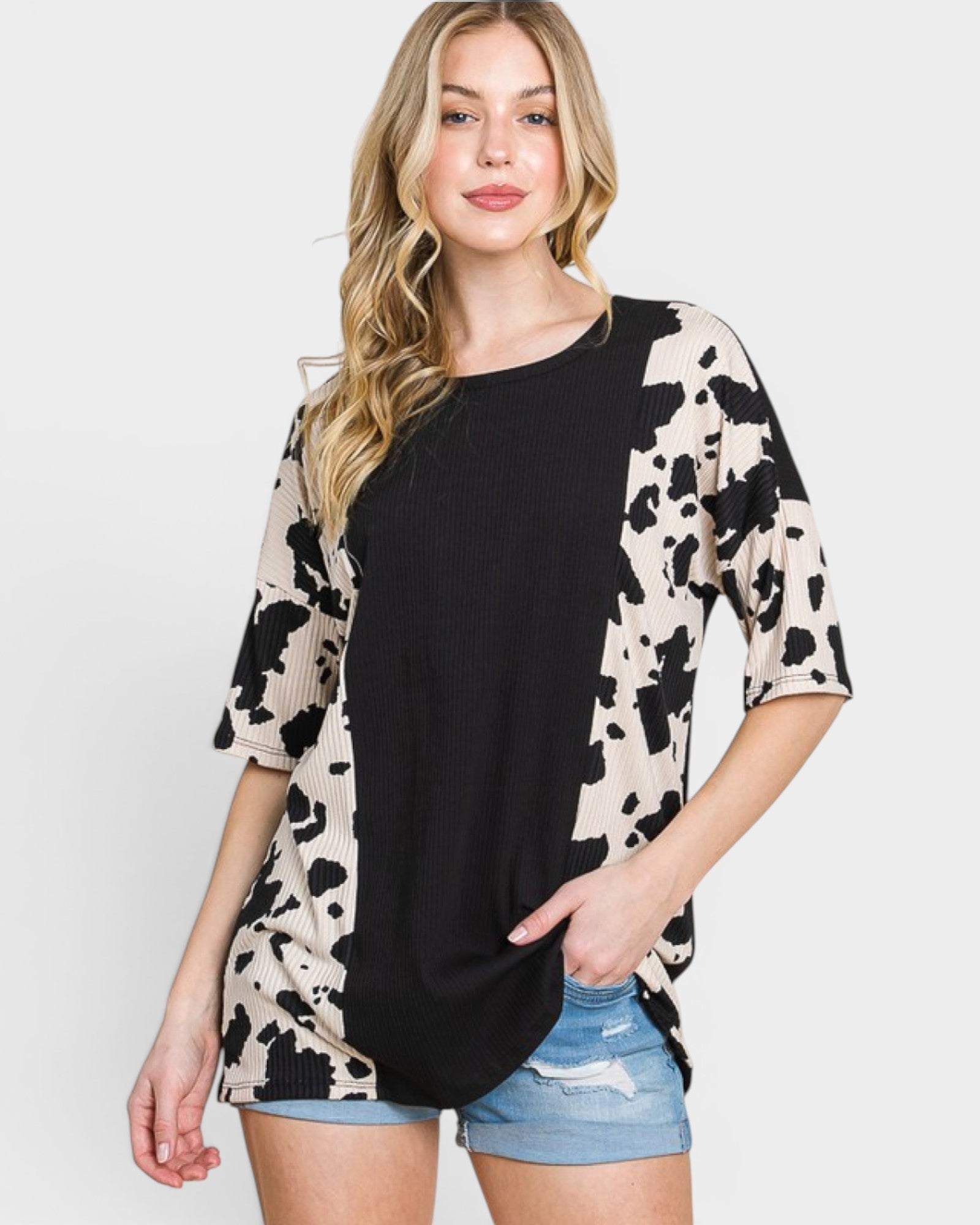 Woman wearing a black and white patterned cardigan over a black top with denim shorts on a plain background
