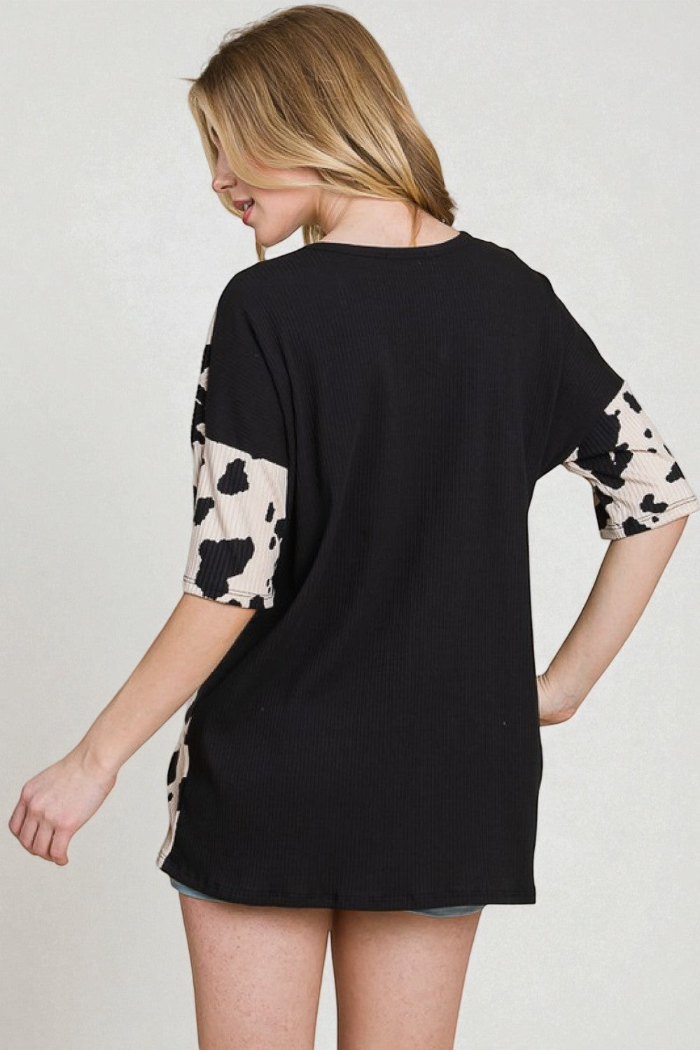 Woman wearing a black t-shirt with cow print sleeves on a plain background
