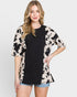 Woman wearing a black top and a beige cardigan with black patterns on a white background