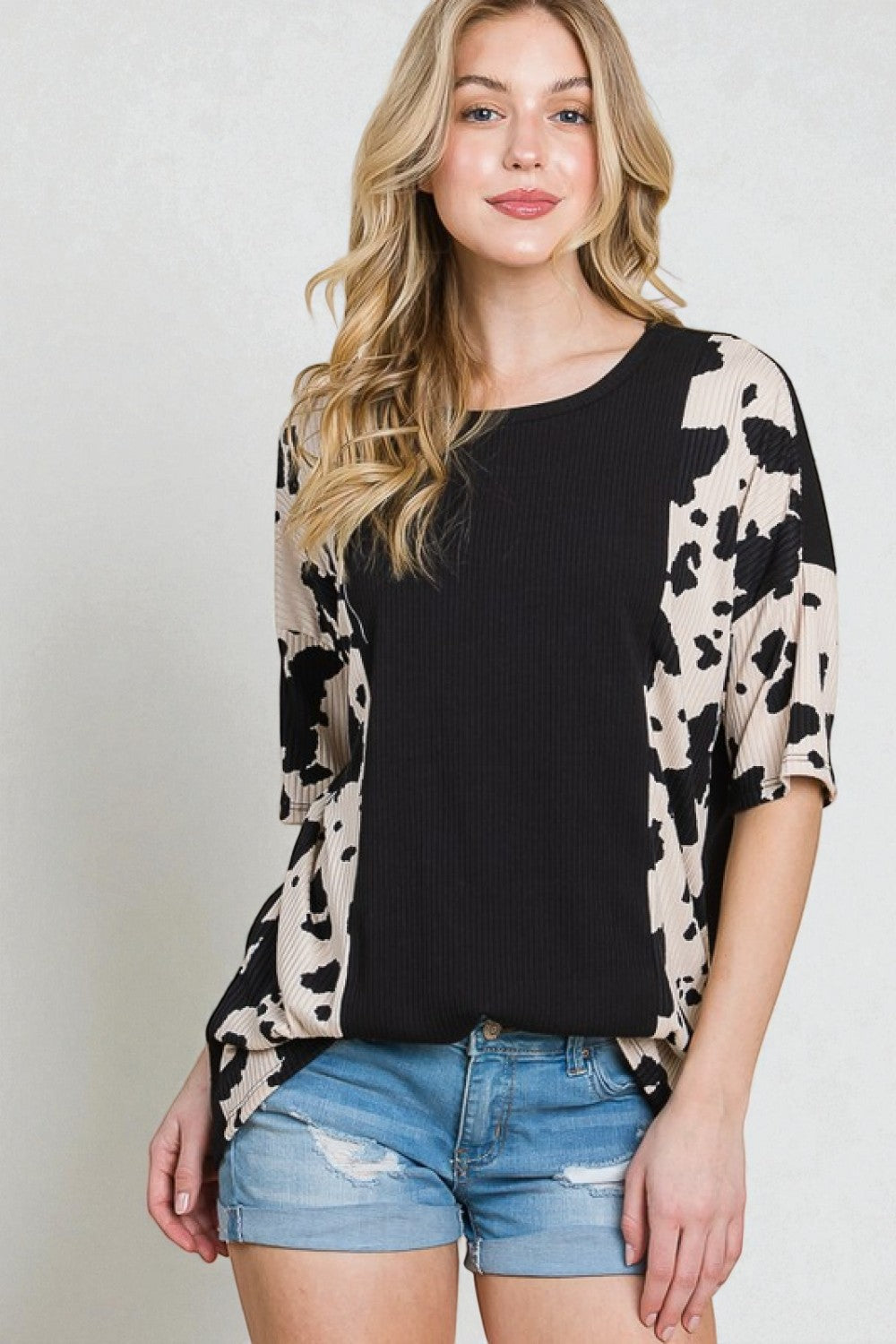 Woman wearing a black top with animal print sleeves and denim shorts on a plain background