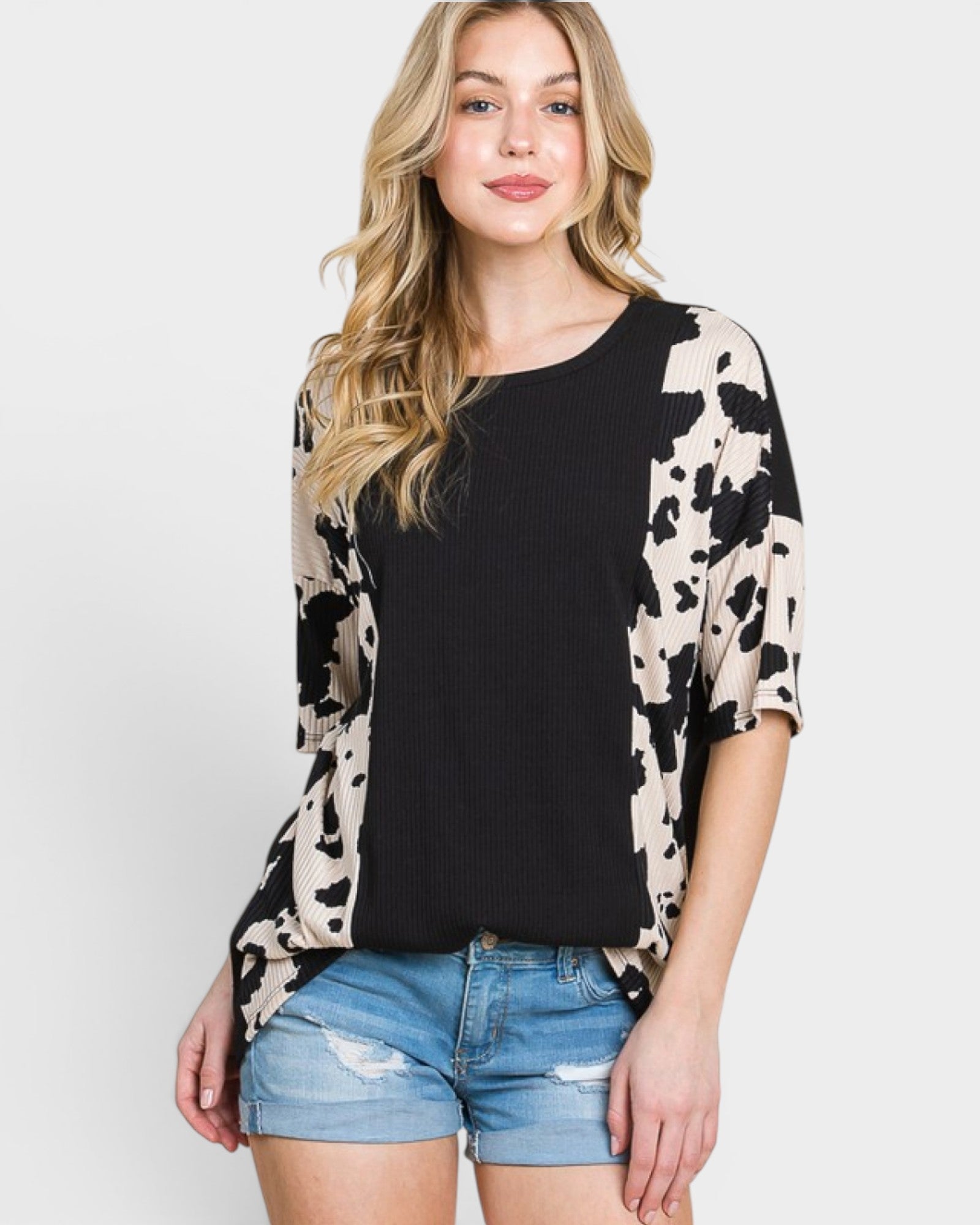 Woman wearing a black and beige patterned top with denim shorts on a white background