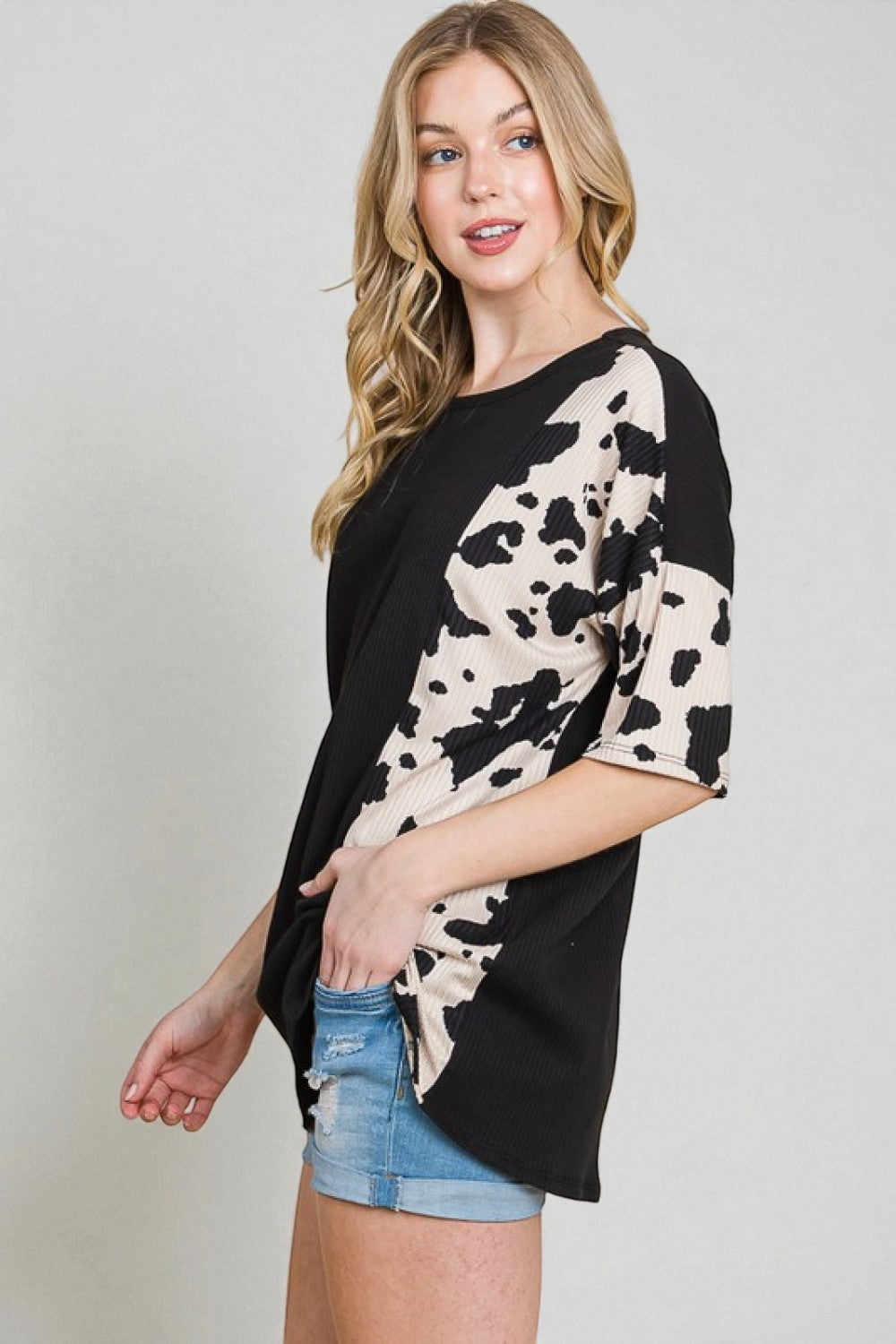Woman wearing a black and white cow print top with denim shorts on a plain background