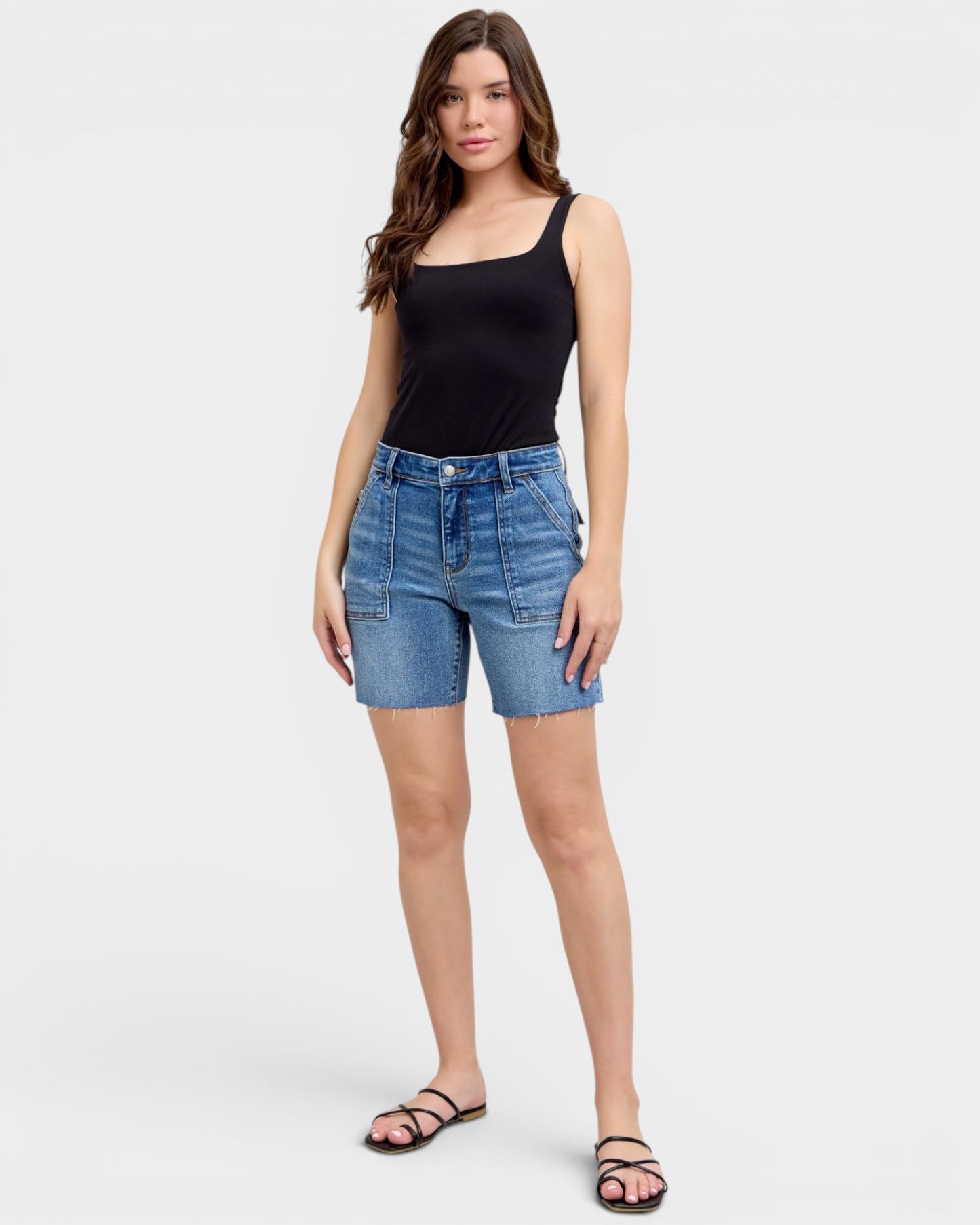 Woman wearing blue denim shorts and a black tank top on a white background