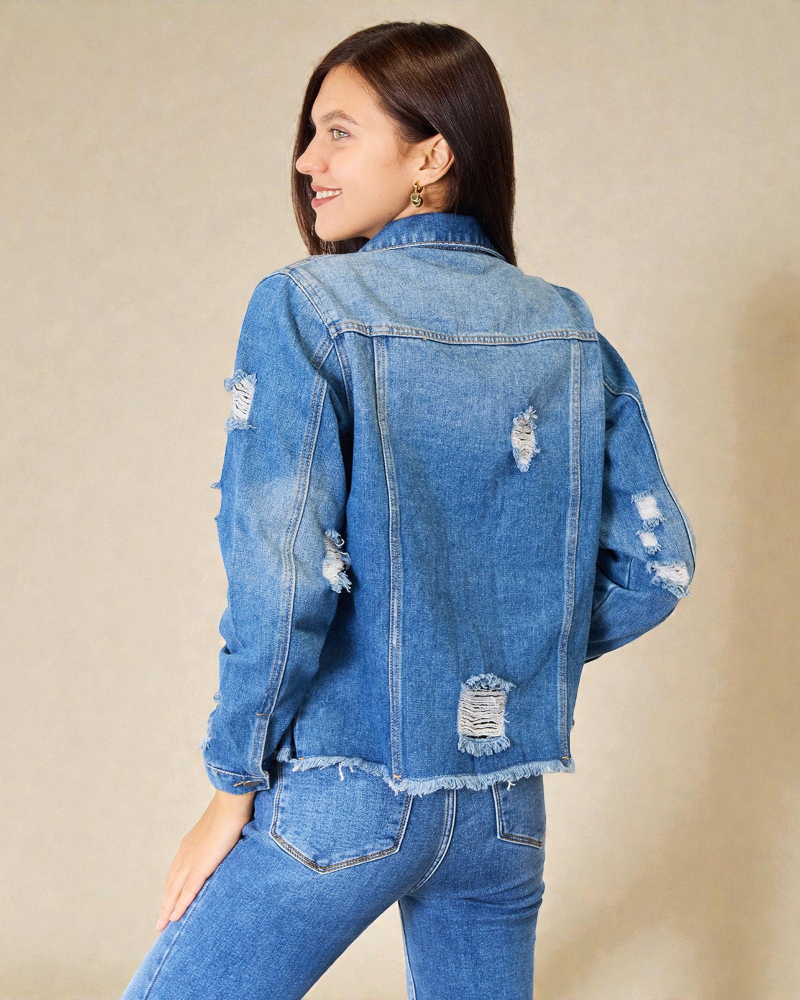Woman wearing a blue denim jacket with distressed details on a beige background