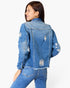 A woman shown from the back wearing a light blue distressed denim jacket and matching blue jeans against a plain white studio background.