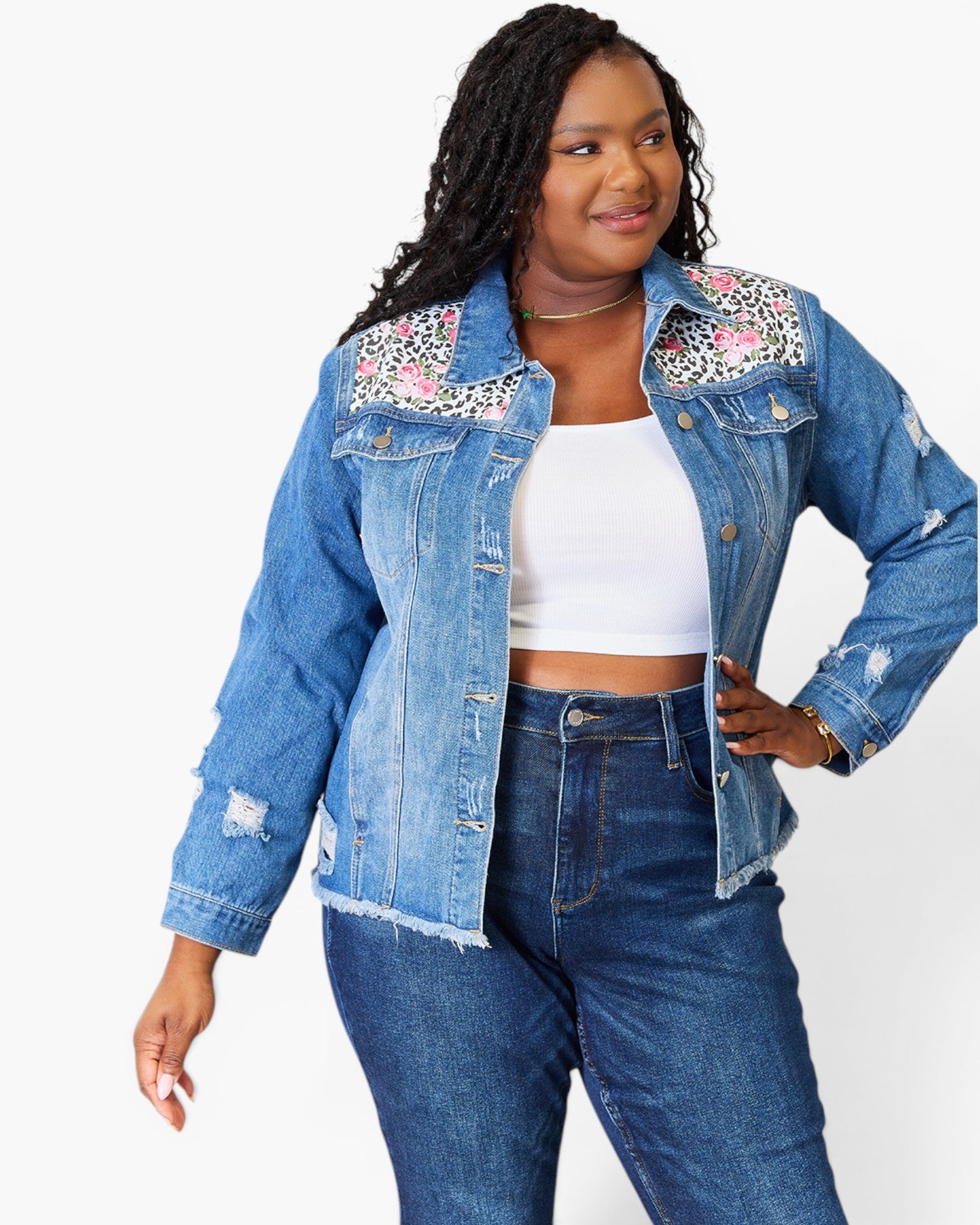 A woman modeling a light blue denim jacket with floral and leopard print embroidery on the shoulders, worn over a white crop top and dark blue jeans against a plain white background.