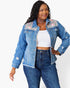 A woman modeling a light blue denim jacket with floral and leopard print embroidery on the shoulders, worn over a white crop top and dark blue jeans against a plain white background.
