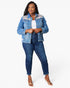A woman modeling a light blue denim jacket with colorful floral embroidery on the shoulders, paired with dark blue jeans and clear high-heeled sandals, against a plain white background.